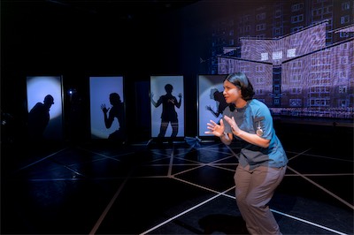 Sangita Baruah as U (foreground), Crosby Lloyd, Jonathan Nathaniel Dingle-El, Nathan Reder, Rachel Fink as Voters (in shadow).